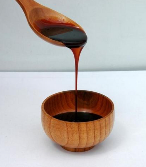 a wooden spoon pouring blackstrap molasses  on a brown bowl